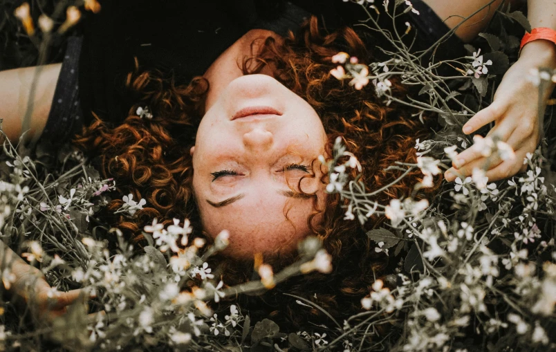 a person laying in grass with flowers around her