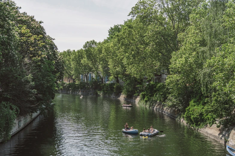 people row boats on the river with a small boat passing by