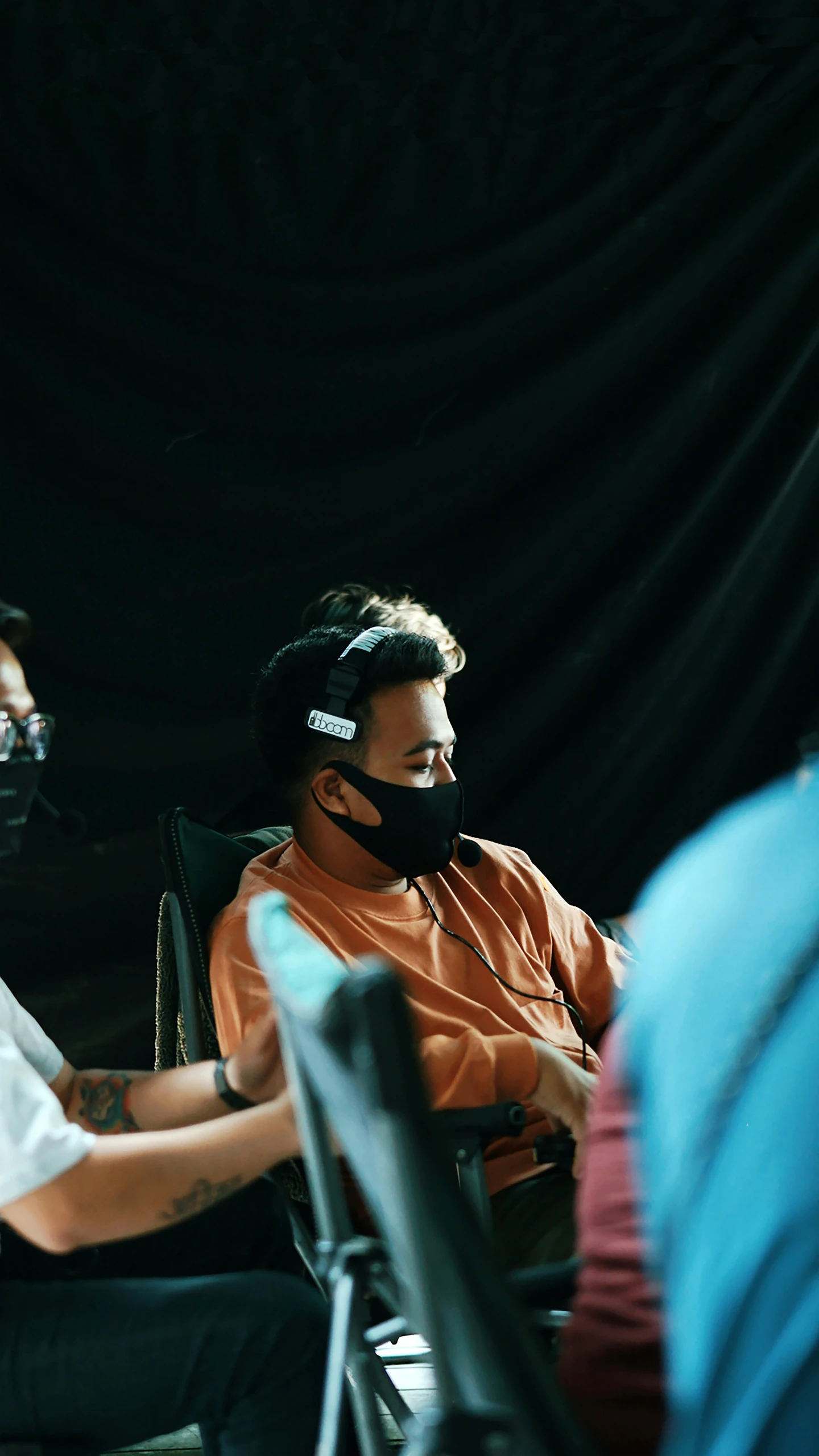 the man wearing the headset is watching another person speak on a microphone