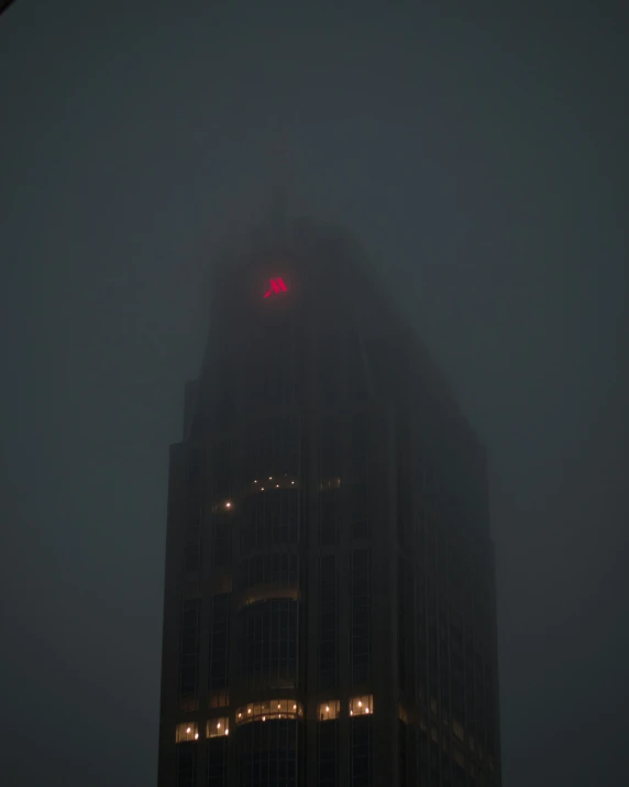 a very large building on a foggy day with a bright red lit cross on top