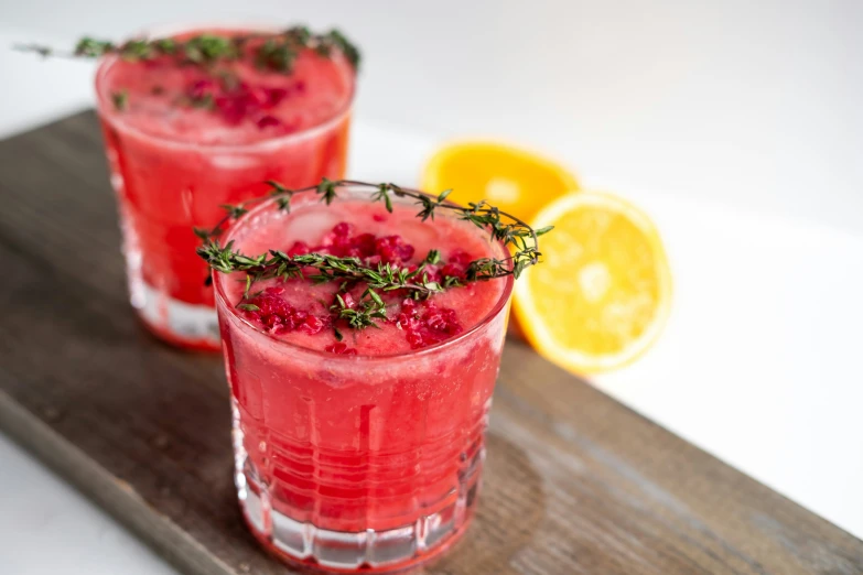 two red glasses sitting on a  board with herbs
