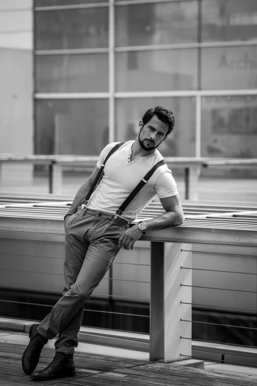 a man leaning on a rail wearing suspenders