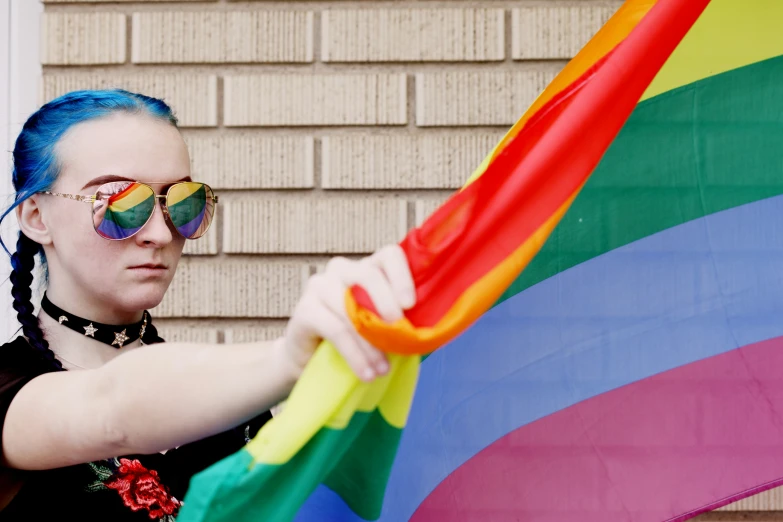 a lady with colorful glasses holding up a rainbow flag