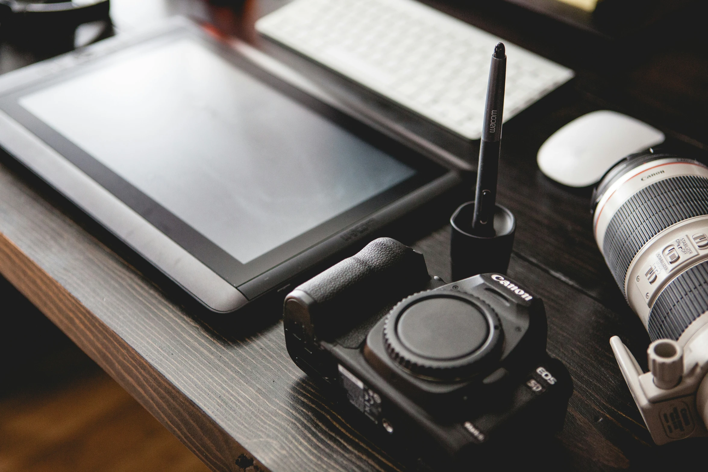 a black tablet, camera, cup and two other things on the desk