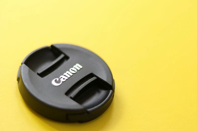 a compact camera lens cap on a yellow surface