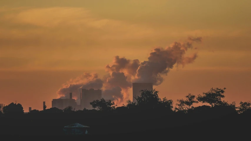 a silhouette of a power plant and trees during sunset