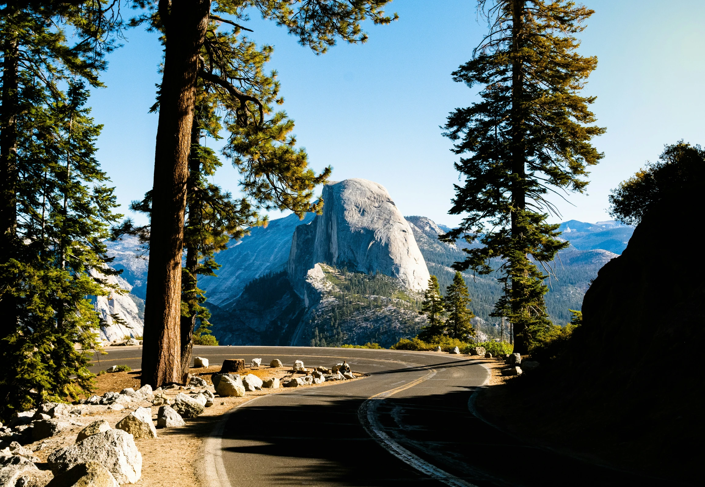 a winding road and tree - lined mountain is shown in the distance