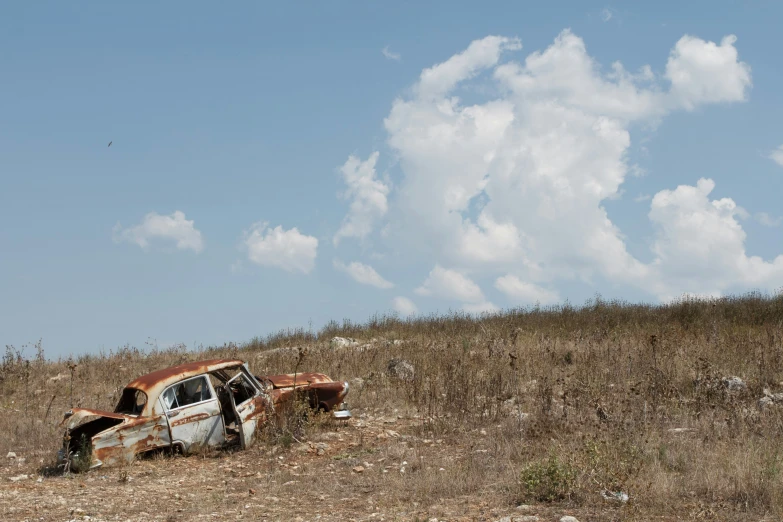 an old abandoned car in a field on a cloudy day