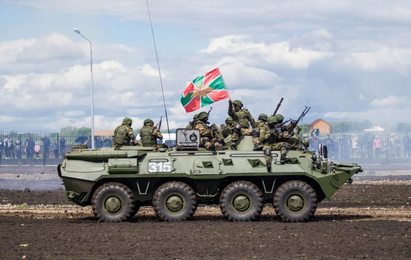 a group of military personnel stand on top of an armored vehicle