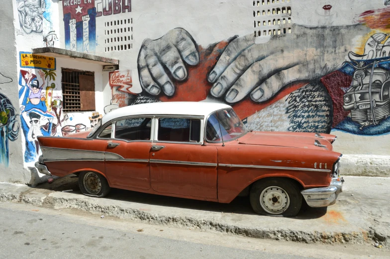 an old red and white car parked in front of a mural