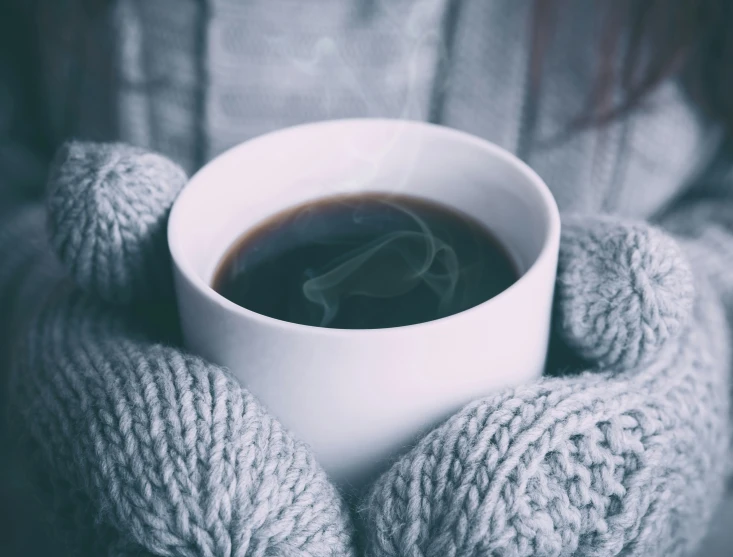 a woman wearing grey gloves holding a coffee cup