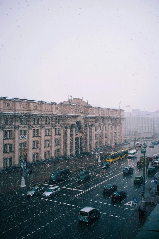 cars are driving in a big city with a light snowing on