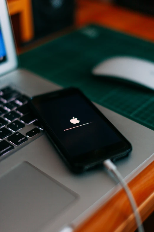 an apple phone on top of the laptop on a desk