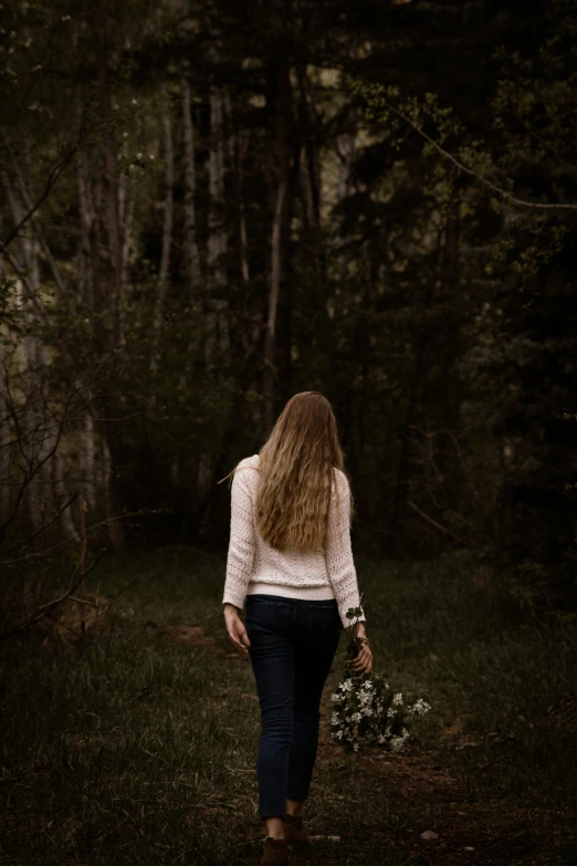 a woman walks through the woods holding a bouquet