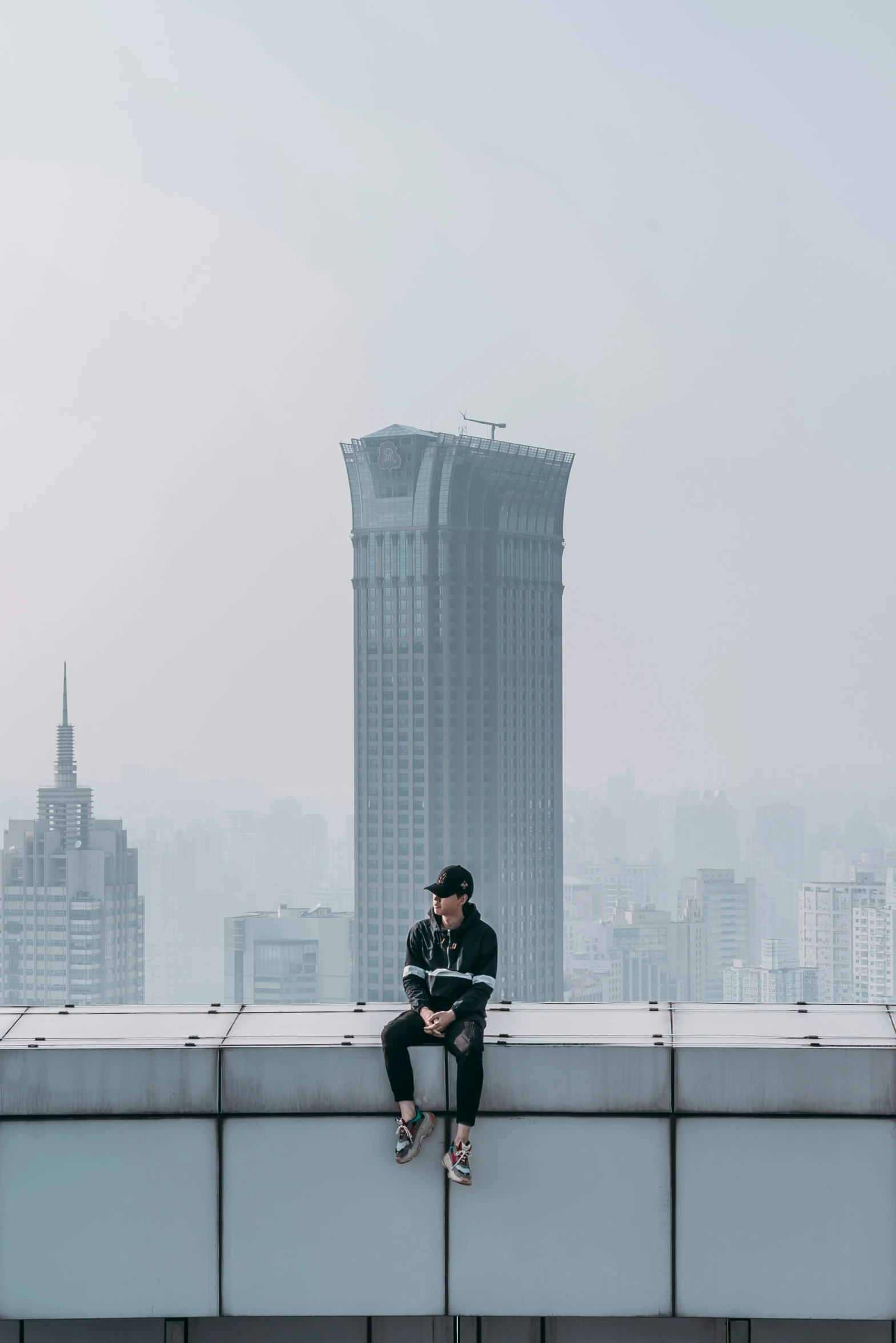 the man is sitting on the ledge of the building overlooking the city