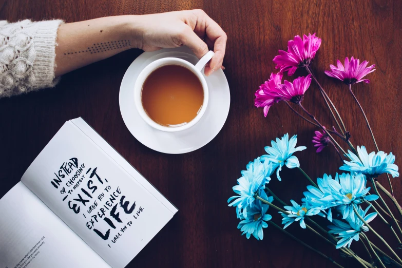 a cup of coffee next to flowers and an open book