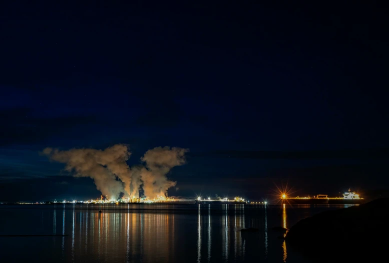 a large factory plant towering over a river at night