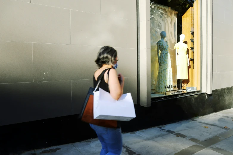 woman carrying shopping bags and walking past a mannequin in a window display