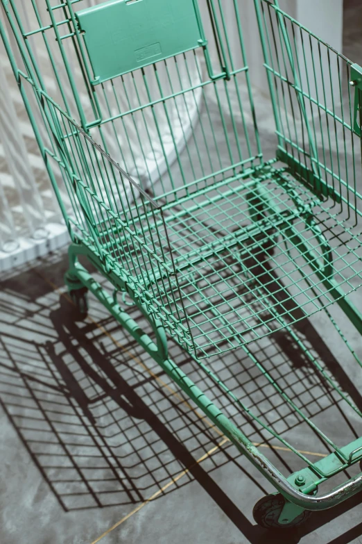 green shopping cart sits in a lot near a wall