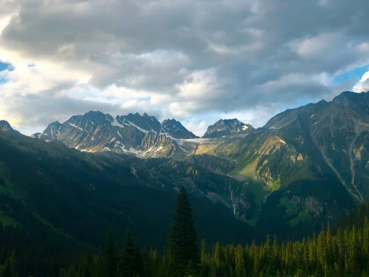 mountain range near lake in forested area under cloudy sky