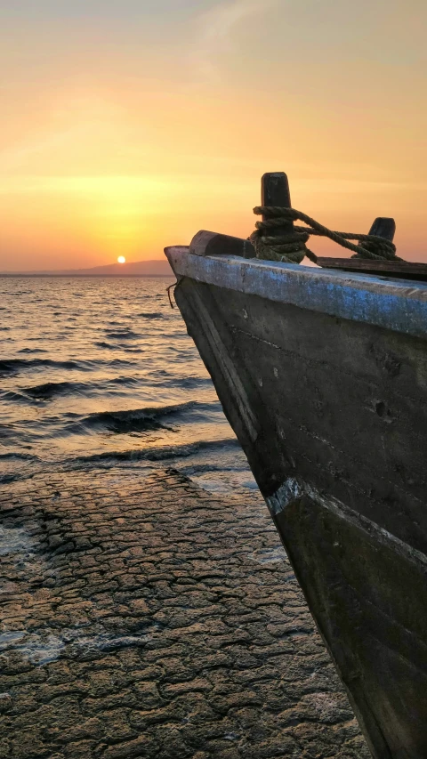 a boat is sitting on the beach at sunset