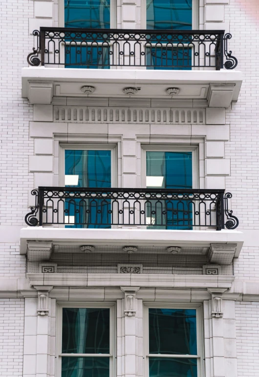 several windows with decorative balconies are seen on a white brick building