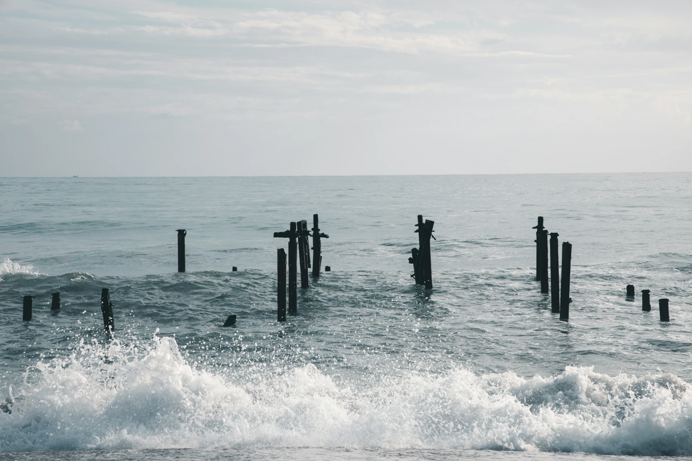 the sea is clear and strong and water has some waves crashing around the posts