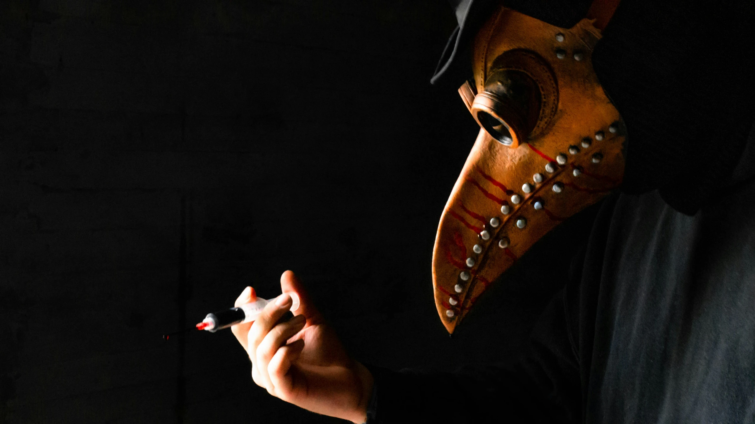 the masked person in a black outfit is holding an electronic cigarette