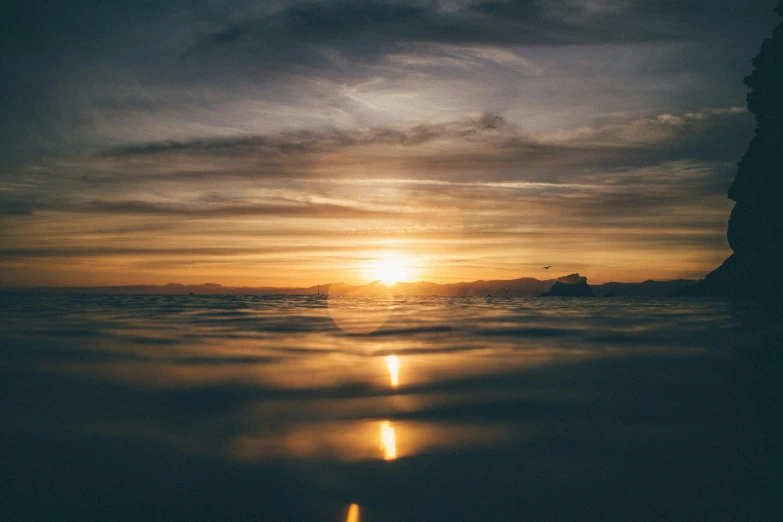 a person standing in front of the sun above the ocean