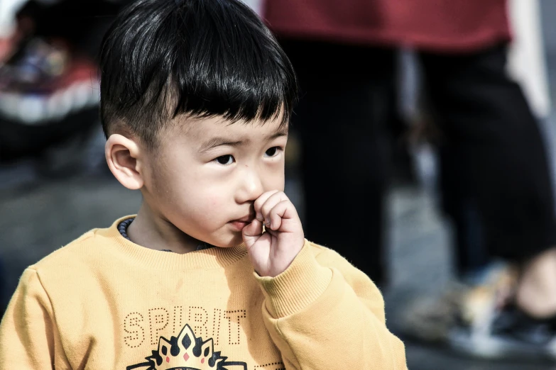 a  in a yellow shirt looks sideways with his hand to his mouth