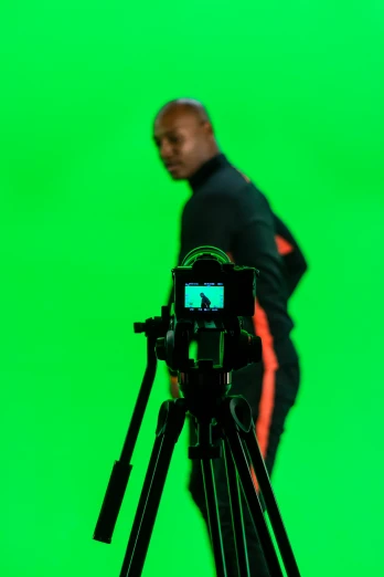 a man stands in front of a green screen behind a tripod