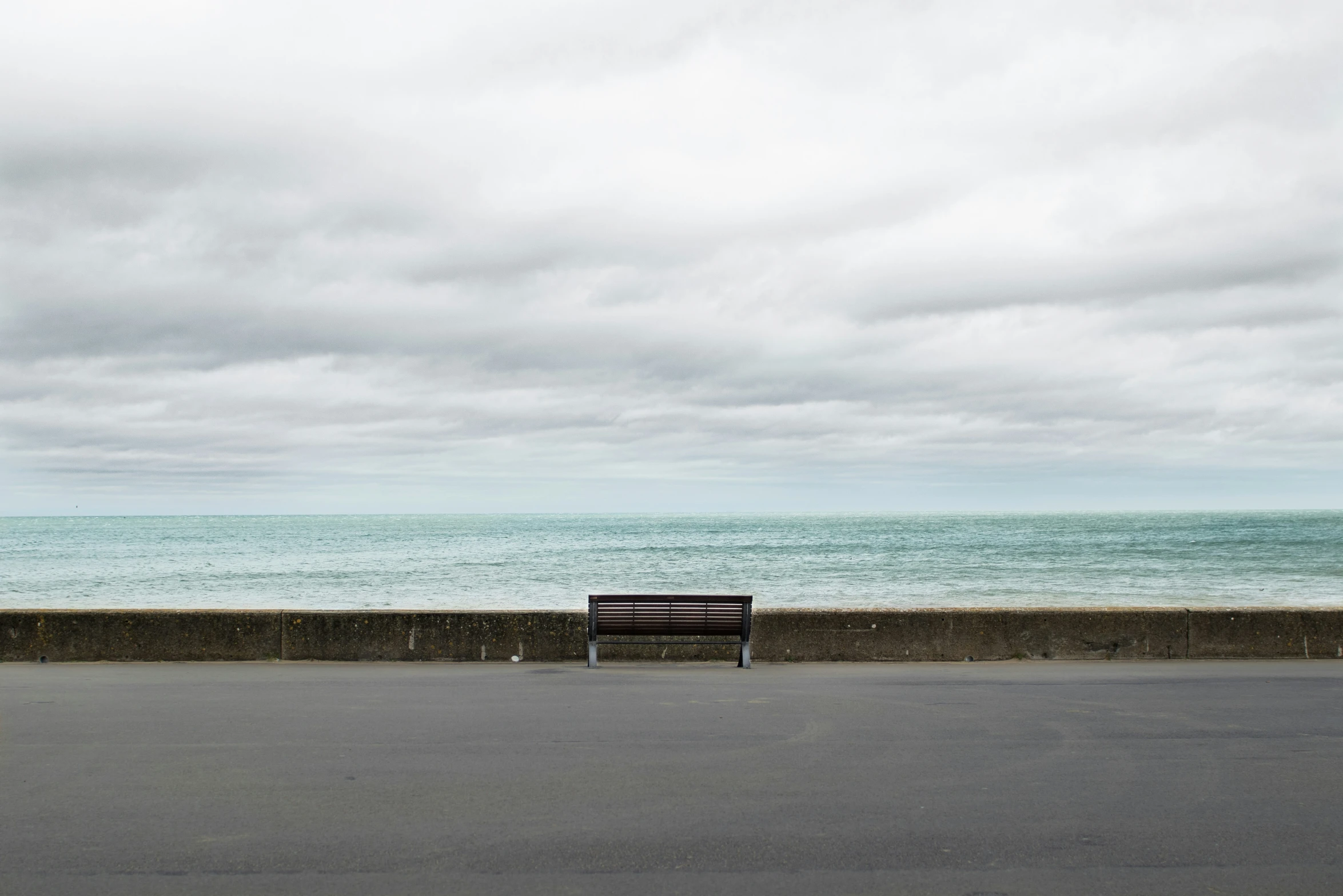 a bench sitting on the side of the road by the ocean