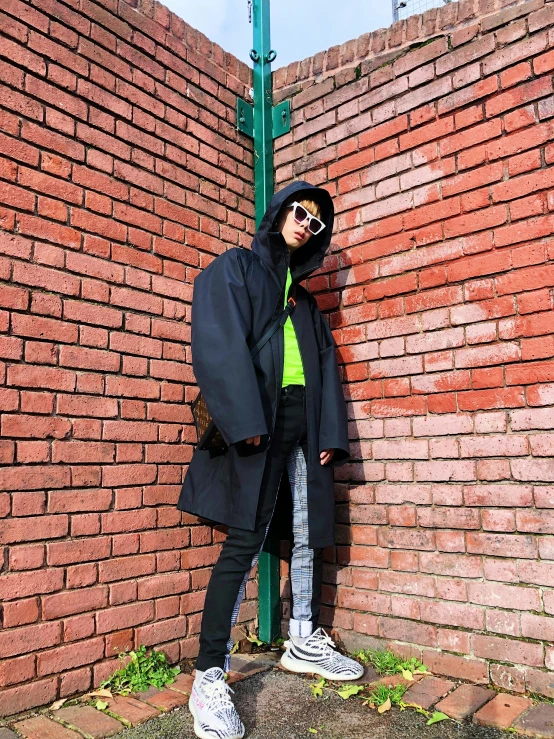 a person wearing glasses leaning against a brick wall