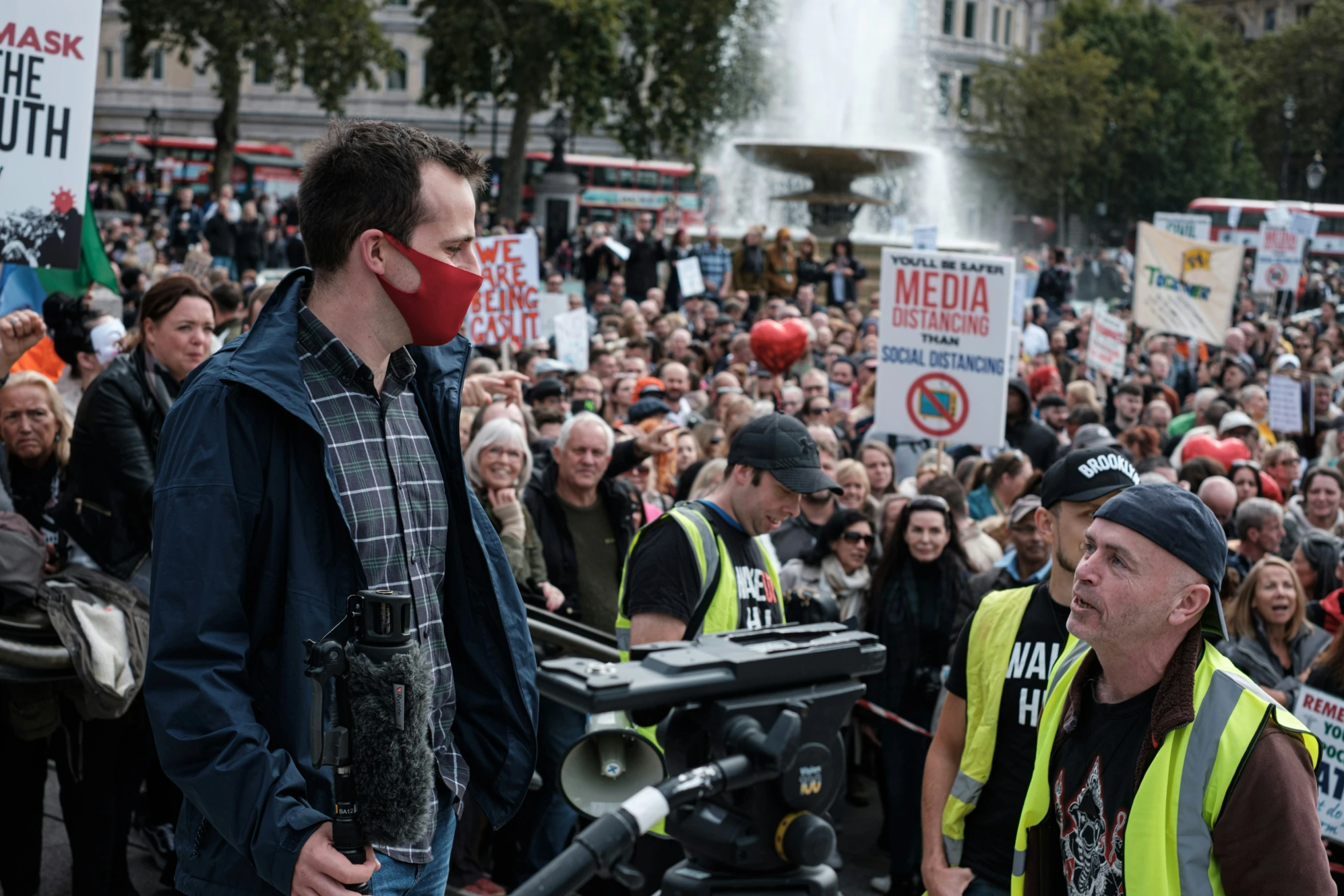 some protesters at a demonstration with a man in a black suit and red mask