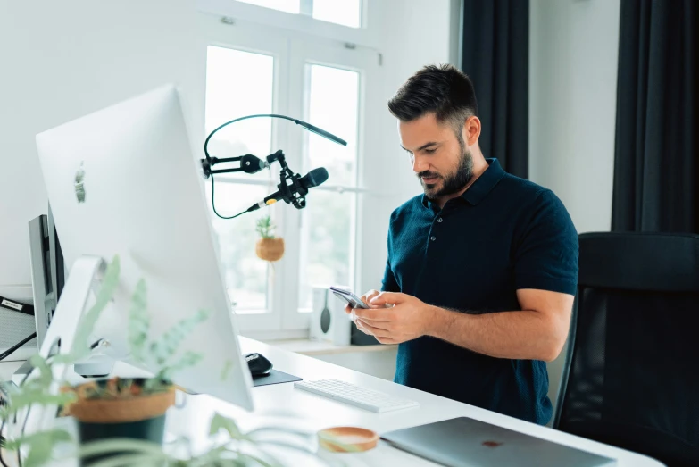 a man looks at his cell phone while standing in front of a computer