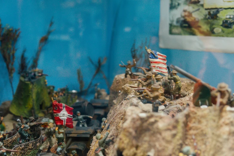 toy army with flags on rocky terrain by blue wall