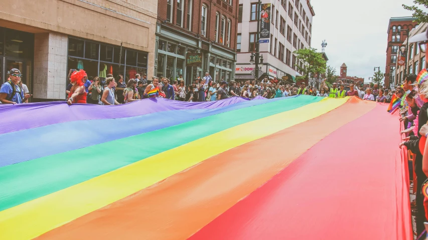 a large rainbow colored kite is being carried by a crowd