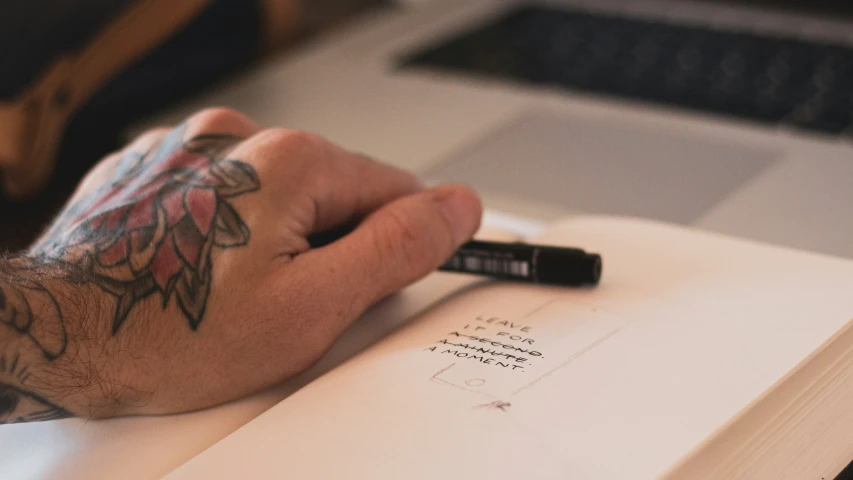 a hand with tattoos is holding an open book