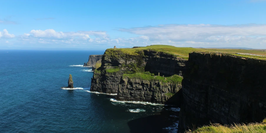 a long cliff with green plants and water below