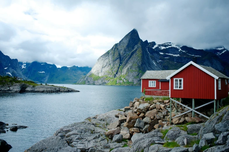 a small red building on the shore in front of mountains