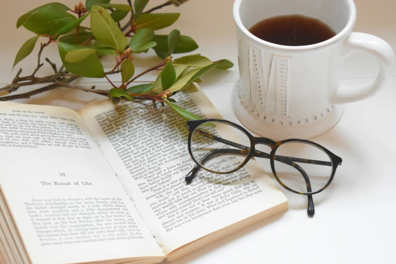 an open book and a pair of eye glasses on a table with coffee