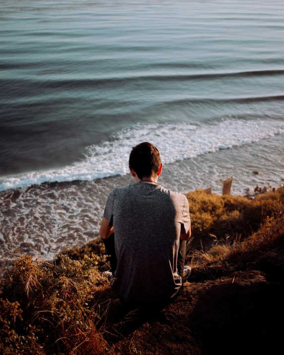 the man is sitting on top of a hill watching the ocean