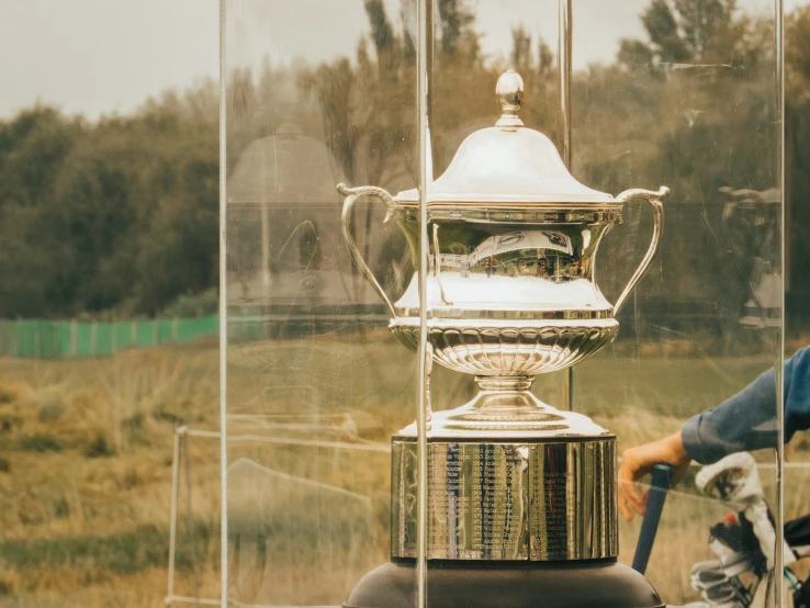 a cyclist riding past a large silver trophy on his bike