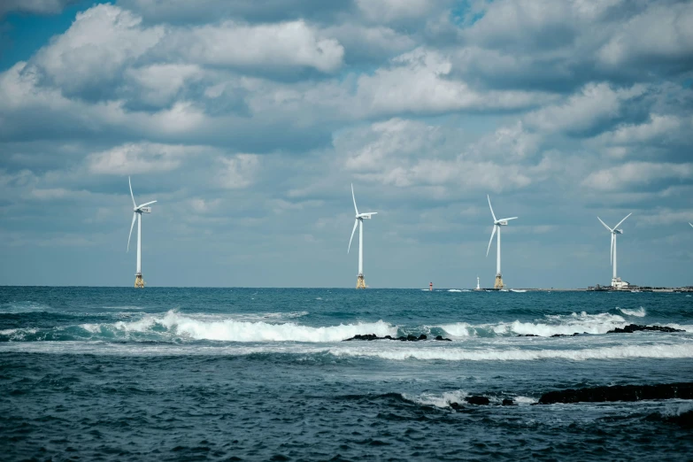 wind generators on the ocean in front of a pier and lighthouse