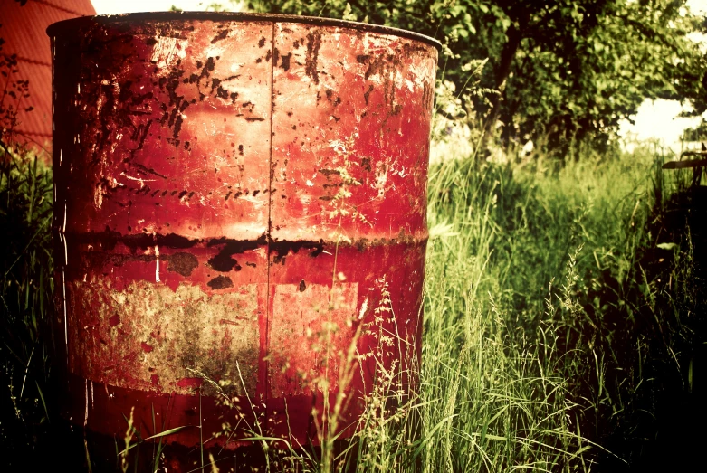 a red trash can sitting in the middle of a field