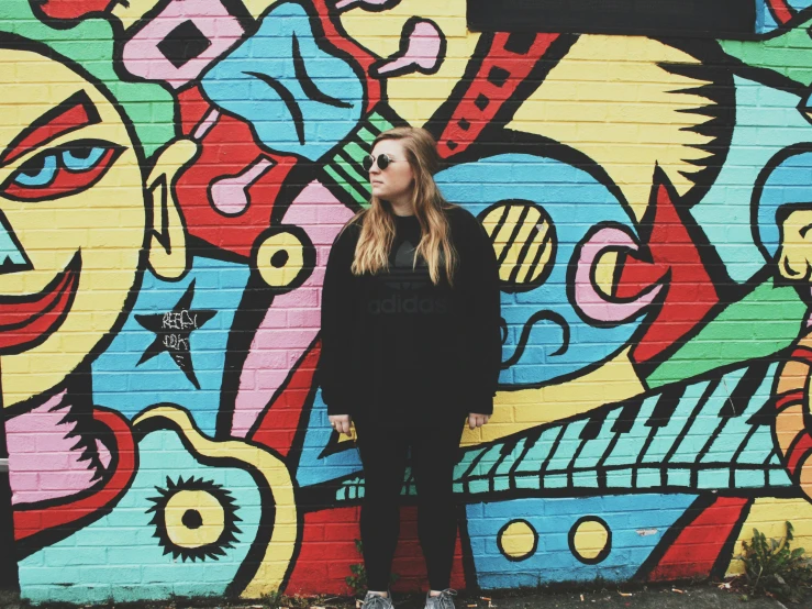 a woman standing against a colorful wall with an abstract painting