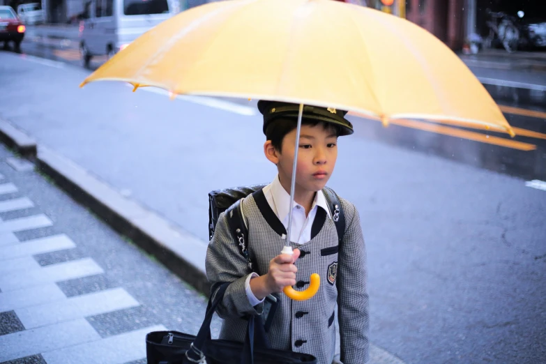 boy wearing hat and plaid jacket holding up yellow umbrella