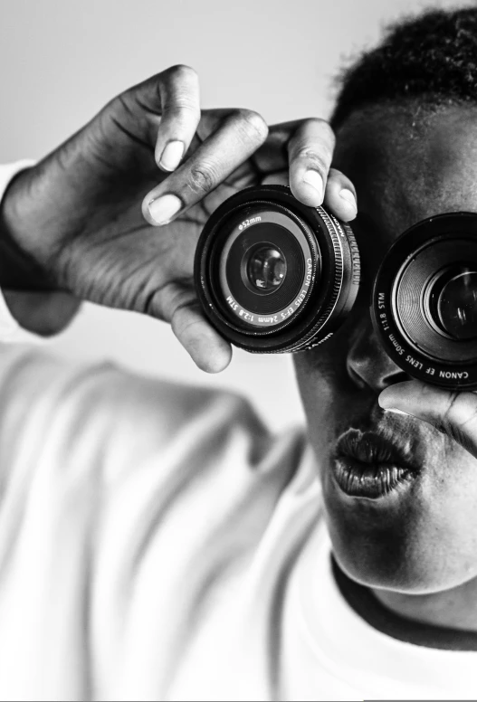 a woman wearing white holds two old camera's up to the eye