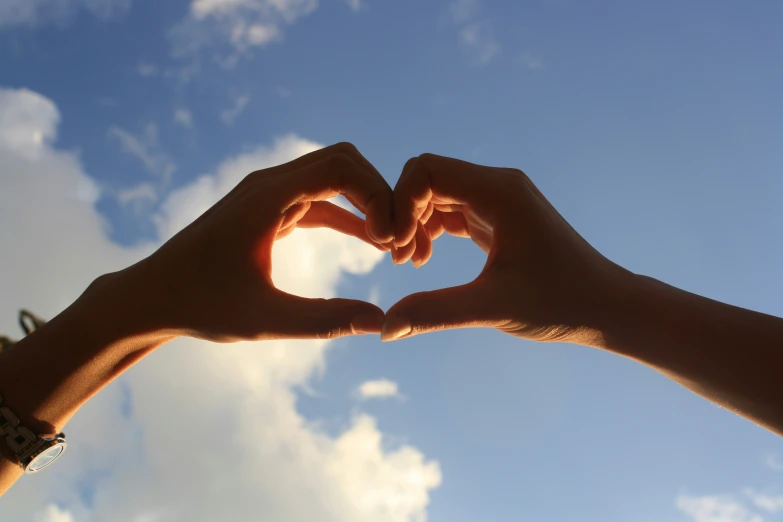 a close up of two people making a heart with their hands