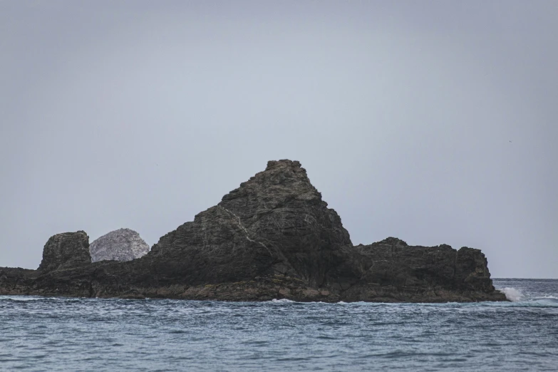a large rock out in the ocean with a bird flying above it